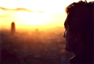 Silhouette of man's head looking at a rising sun over an indeterminate landscape.